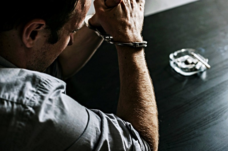 Handcuffed man beside cash on wooden table