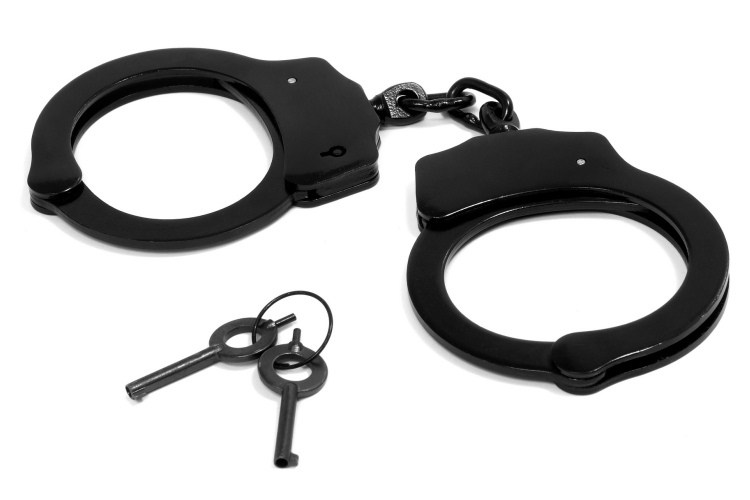 Pair of closed black handcuffs and two keys on adjacent keyring pictured against white background