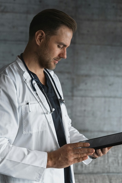 Doctor in labcoat reviewing tablet screen beside concrete wall